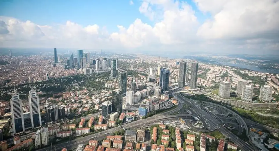 Aerial view of a modern city with skyscrapers, residential blocks, and a cloverleaf highway interchange.