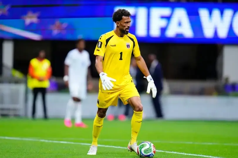 Goalkeeper in yellow kit with number 1 and white gloves controlling a soccer ball on a green field.